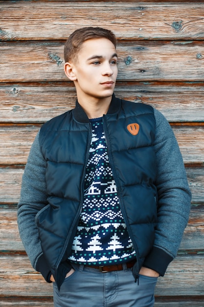 Handsome young man in a knitted sweater and winter warm jacket near the vintage wooden wall