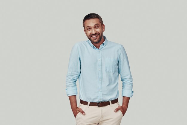 Handsome young man looking at camera and smiling while standing against grey background