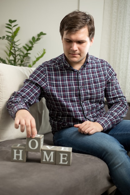 Handsome young man making word "Home" from letters on cubes