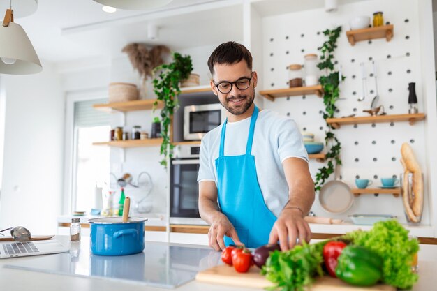 Handsome young man man stand at modern kitchen chop vegetables\
prepare fresh vegetable salad for dinner or lunch young male\
cooking at home make breakfast follow healthy diet vegetarian\
concept