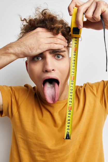 Handsome young man measuring tape measure in yellow tshirt light background