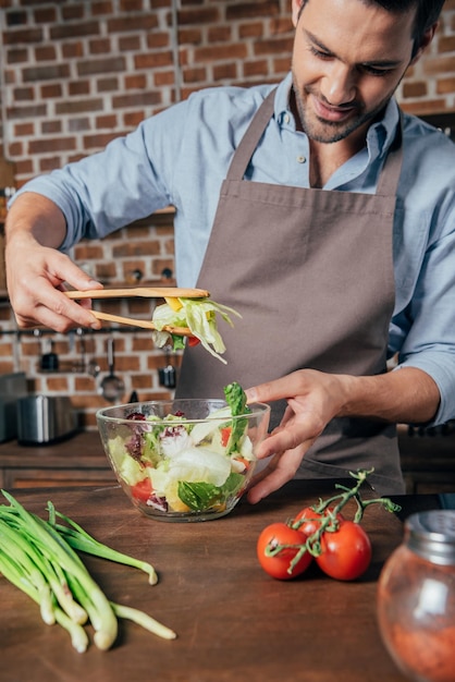 Handsome young man mixing salad