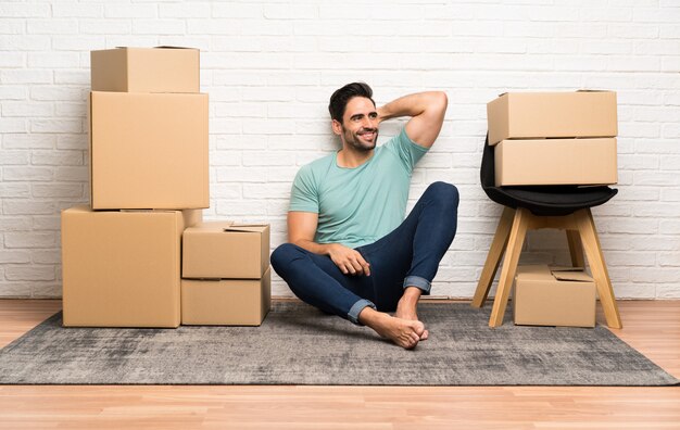 Photo handsome young man moving in new home among boxes laughing