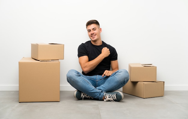 Handsome young man moving in new home among boxes celebrating a victory