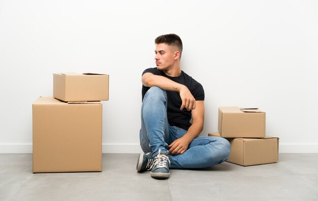 Handsome young man moving in new home among boxes looking side