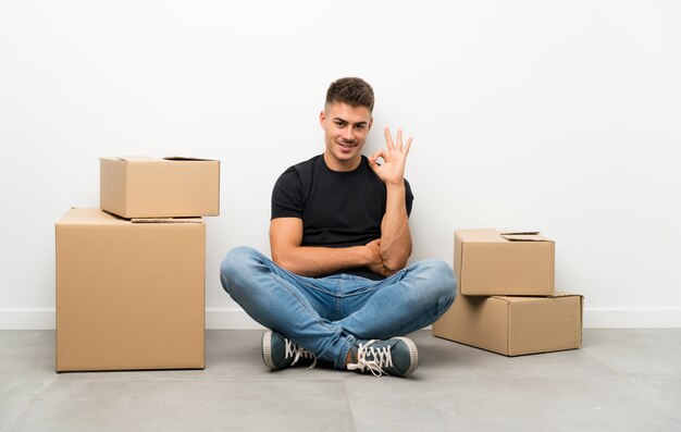 指でokの標識を示すボックスの間で新しい家に移動するハンサムな若い男