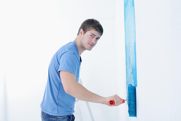 handsome young man paint in blue and green color  white wall of new home