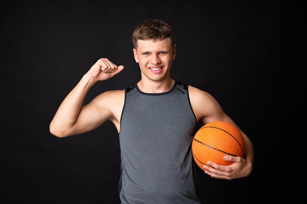 Handsome young man playing basketball over isolated black wall