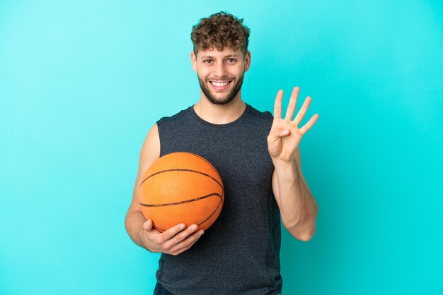 Handsome young man playing basketball isolated on blue background happy and counting four with fingers