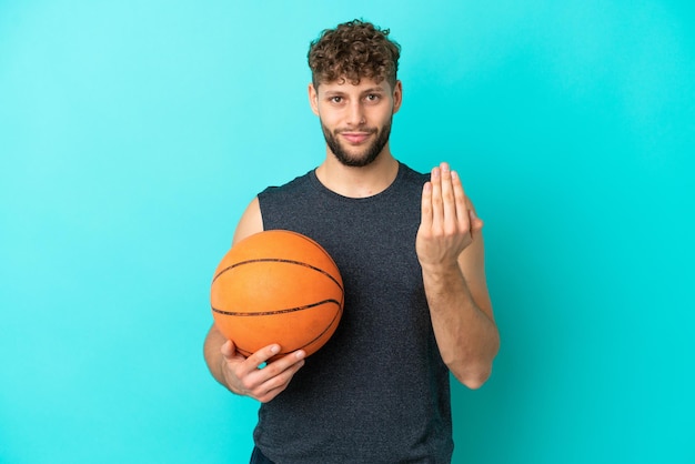 Красивый молодой человек играет в баскетбол, изолированные на синем фоне, приглашая прийти с рукой. Счастлив что ты пришел