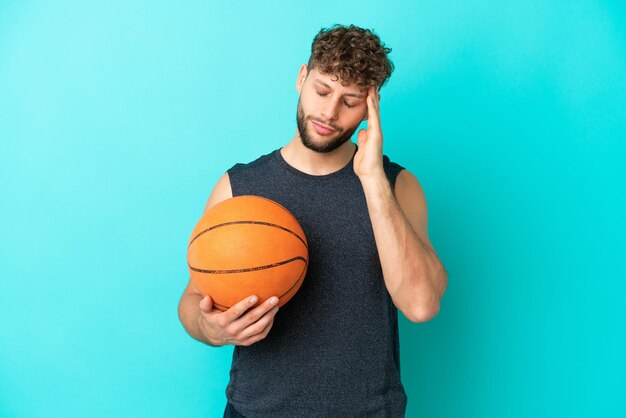 Handsome young man playing basketball isolated on blue background with headache