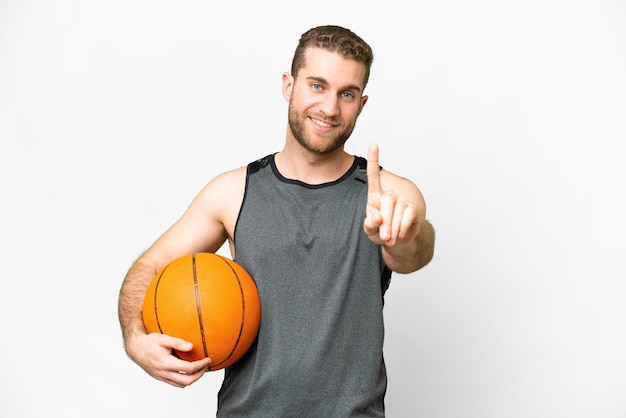 Красивый молодой человек играет в баскетбол на изолированном белом фоне, показывая и поднимая палец