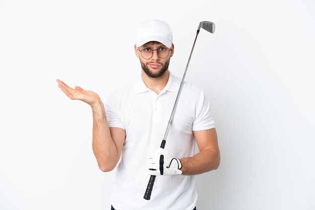 Красивый молодой человек, играющий в гольф на белом фоне, сомневается, поднимая руки