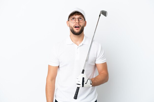 Handsome young man playing golf  isolated on white background looking up and with surprised expression