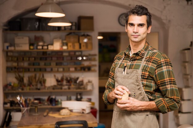 Handsome young man in pottery workshop holding clay