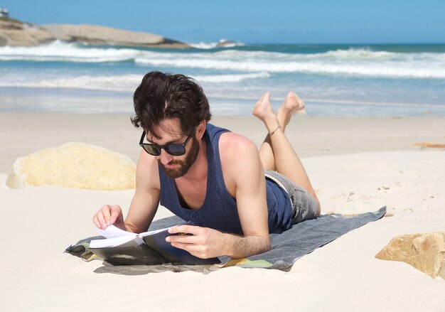 Handsome young man reading book at the beach