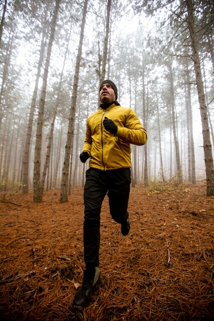 Handsome young man running in autumn forest and exercising for trail run marathon endurance race