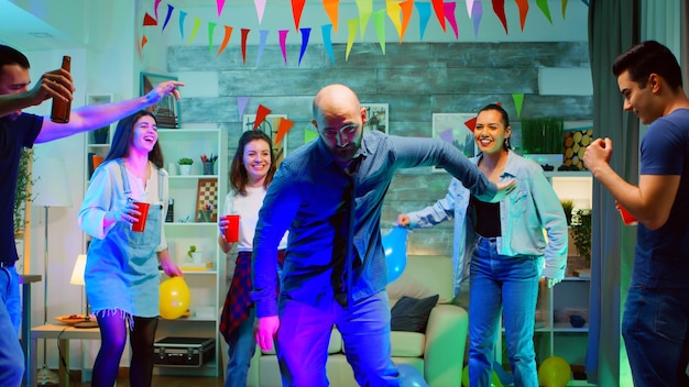 Bel giovane che mostra le sue mosse di ballo ai suoi amici alla festa in un appartamento con luci al neon. robot dance a una festa in discoteca sfrenata
