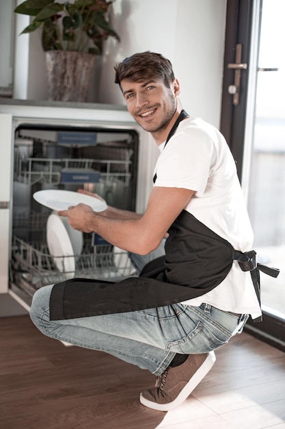 Handsome young man sitting near an open dishwasher