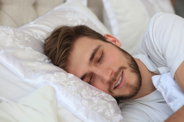 Handsome young man sleeping in white bedding.