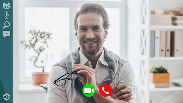 Photo handsome young man smiling and looking at camera while having video call