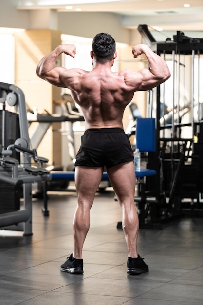 Handsome Young Man Standing Strong In The Gym And Flexing Muscles Muscular Athletic Bodybuilder Fitness Model Posing After Exercises