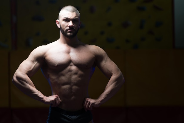 Handsome Young Man Standing Strong In The Gym And Flexing Muscles  Muscular Athletic Bodybuilder Fitness Model Posing After Exercises