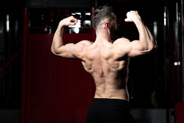 Handsome Young Man Standing Strong In The Gym And Flexing Muscles - Muscular Athletic Bodybuilder Fitness Model Posing After Exercises