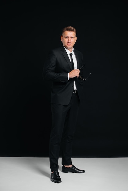 A handsome young man in a stylish black suit poses on a black background. A stylish business man. A big businessman.