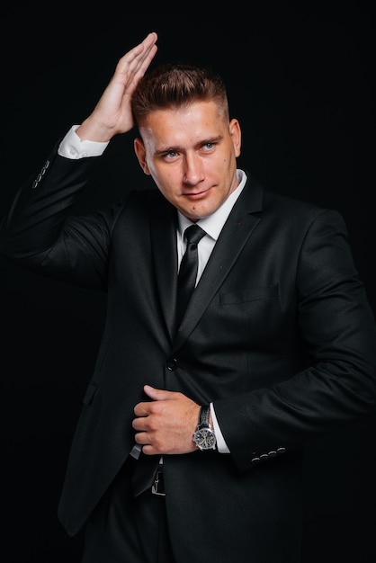 A handsome young man in a stylish black suit poses on a black background. A stylish business man. A big businessman.