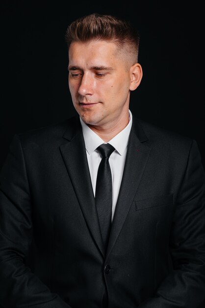 A handsome young man in a stylish black suit throws money dollars on a black background.

