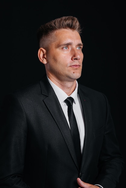 A handsome young man in a stylish black suit throws money dollars on a black background.

