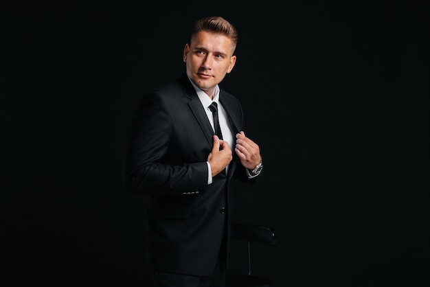 A handsome young man in a stylish black suit throws money dollars on a black background.

