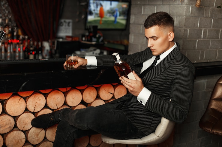 Photo handsome young man in a stylish suit holding a bottle of whiskey at the bar