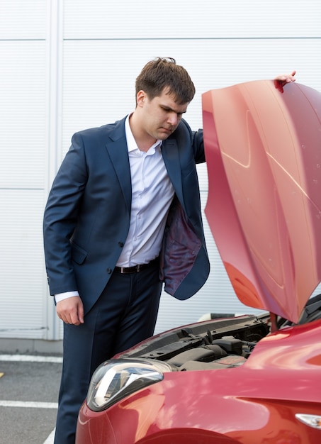 壊れた車のボンネットの下を見てスーツを着たハンサムな若い男