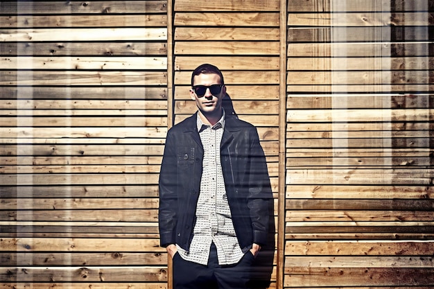 Handsome young man in sunglasses and a black jacket on a wooden background