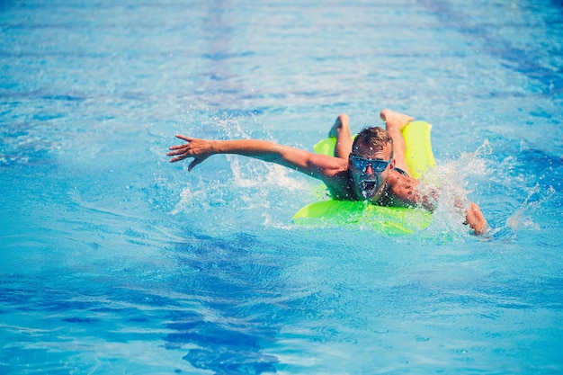 ハンサムな若い男は青いプールで膨脹可能なマットレスで泳ぐ