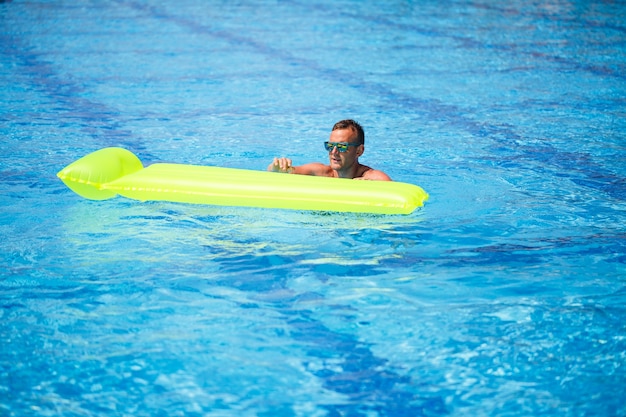 Handsome young man swims on inflatable mattress in blue pool