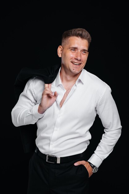 A handsome young man takes off his jacket and laughs posing on a black background. A stylish business man. A big businessman.