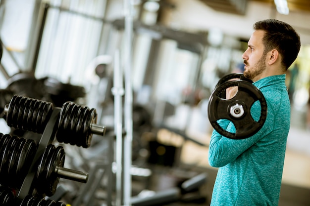 Handsome young man uses dumbbells in gym