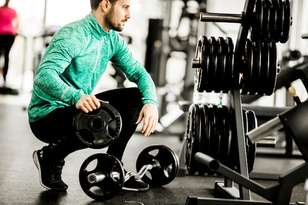 Handsome young man uses dumbbells in gym