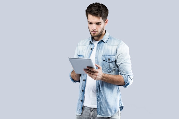 Handsome young man using his digital tablet over gray background.