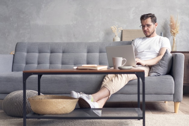 Handsome young man using his laptop with smile while sitting on the couch at home