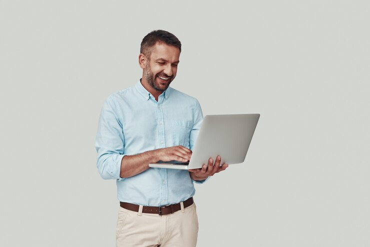 Photo handsome young man using laptop and smiling while standing against grey background