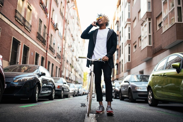 Bel giovane utilizzando il telefono cellulare e la bicicletta a scatto fisso in strada.