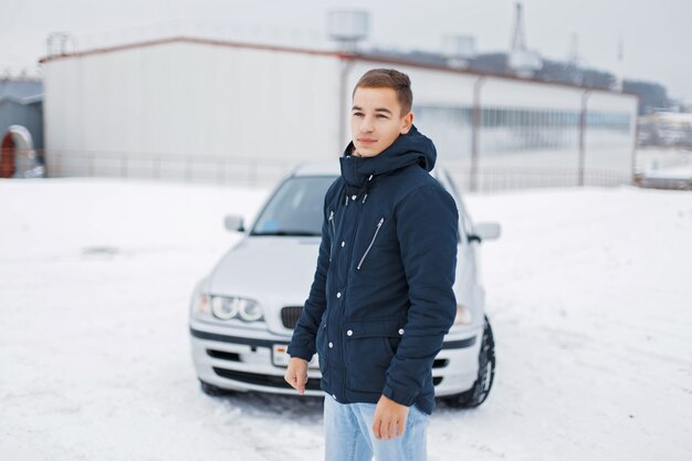 Handsome young man in warm clothes posing on the background of cars