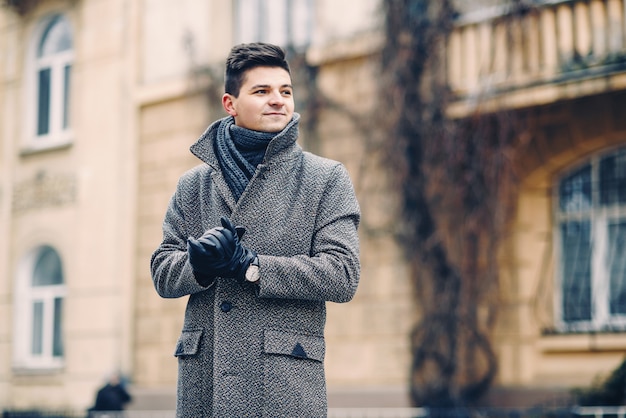 A handsome young man in a warm coat, leather gloves with a\
watch on a city walk