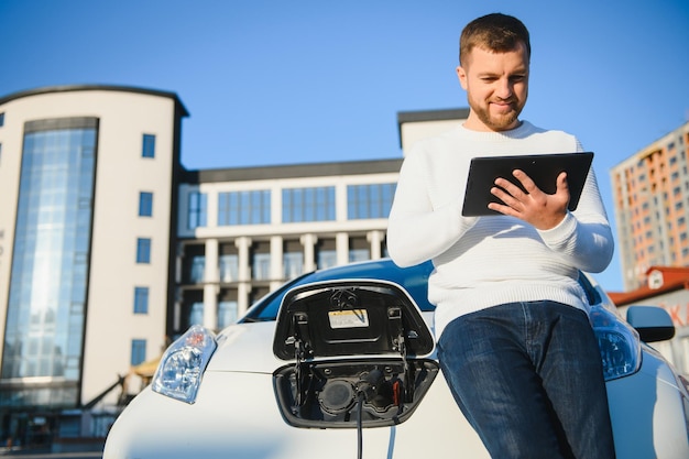 彼の車の充電を見ているハンサムな若い男