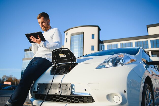 彼の車の充電を見ているハンサムな若い男