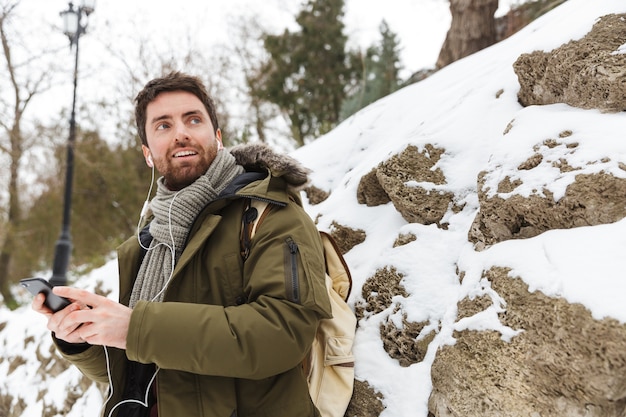 handsome young man wearing winter jacket using mobile phone while walking outdoors